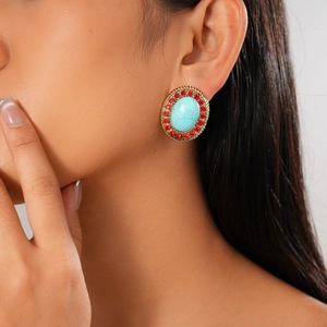 Close-up of bohemian gold earrings with turquoise stone and red rhinestones on a model