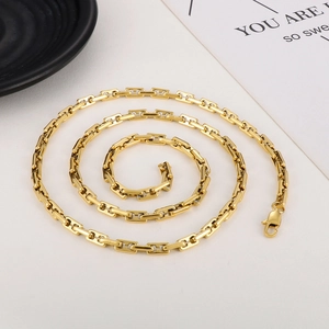 Detail shot of golden geometric link chain necklace coiled on a white surface