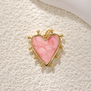 Macro shot of gold-plated heart pendant with pink pearlescent enamel and bead trim