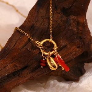 Gold beaded necklace with red coral, seashell pendants and charms on dark wood base