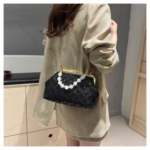 Detail of a black quilted sequin crossbody bag with pearl handle and golden chain on model