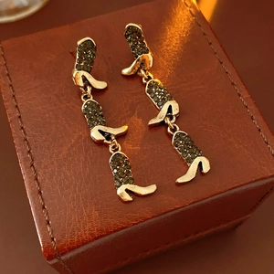 Macro detail of gold-tone boot-shaped fringe earrings with inlaid rhinestones on leather