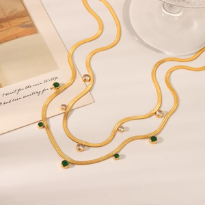 Detail view of 18K gold snake chain with green emerald-style stones and white zircons