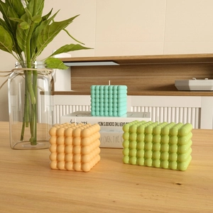 Dettaglio di candele profumate bubble cube verdi e arancioni su un tavolo di legno