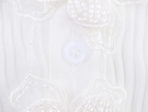 Detail der weißen Plissee-Bluse mit Stickerei, Perlenbesatz und Knopfverschluss