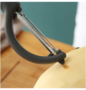 Close-up of multifunctional kitchen peeler removing skin on a wooden board