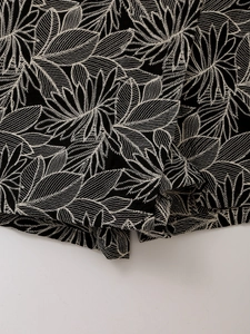 Detailed close-up of white leaf embroidery on premium black cotton fabric surface