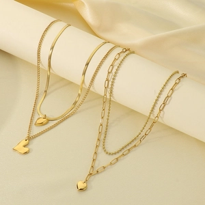 Close-up of golden layered heart necklace with snake and paperclip chains on silk