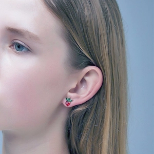 Close-up of a cute red strawberry stud earring worn by a model on a light blue background