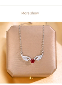 Macro shot of silver wing necklace featuring a red heart zircon on a gold jewelry box