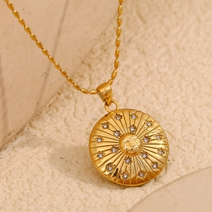 18K gold plated sun face medallion necklace with sparkling gems on a beige surface