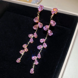 Détail de boucles d'oreilles en zircon rose avec pompon doré dans une boîte noire