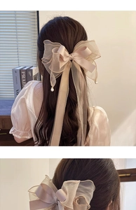 Detail of oversized champagne satin bow hair clip with elegant pearl charms on ribbons