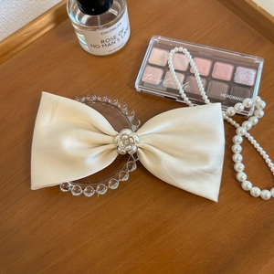 Detail of a beige satin bow hair clip with pearl flower center on a wooden tray