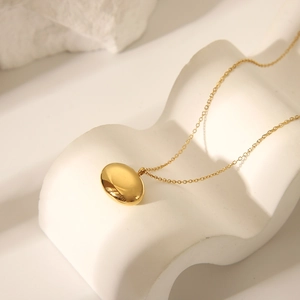 Gros plan d'un collier doré avec pendentif ovale poli sur un support en pierre blanche