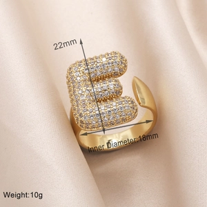 Macro shot of gold letter E ring featuring zircon pavé settings on satin background