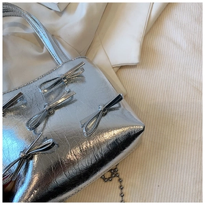 Detail of silver handbag featuring shiny pleated texture and metallic bow decorations