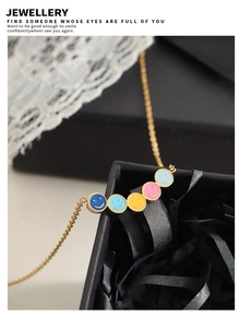 Dettaglio di una collana d'oro con cinque ciondoli smiley colorati su un portagioie
