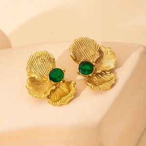 Detailed view of gold flower earrings with radial textures and emerald green gemstones