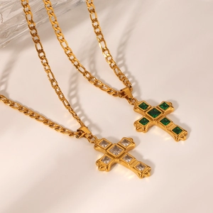 Detail of gold Figaro chains with cross pendants featuring clear and emerald green zircons