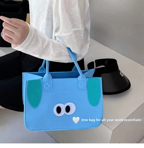 Detail of light blue felt tote bag featuring cute cartoon eyes and plush floppy dog ears