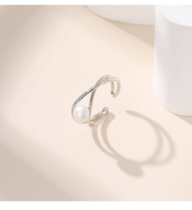 Detail view of a silver crossover open ring featuring a white pearl on a beige background
