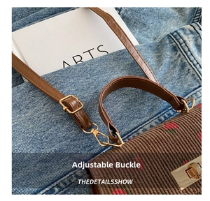 Close-up of adjustable strap buckle and red strawberry embroidery on brown corduroy bag