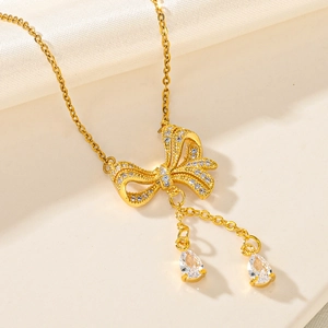 Detail shot of golden bow necklace with pave zircon and pear-shaped drops on white silk