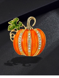 Close-up of Halloween pumpkin brooch with orange enamel, green leaves and white crystals