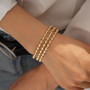 Dettaglio di un set di tre braccialetti con sfere dorate in stile minimalista