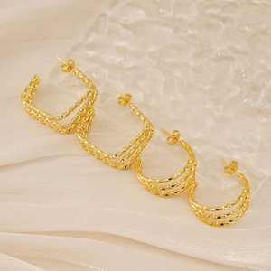 Macro shot of 18K gold plated twisted hoop earrings on wavy glass and silk fabric