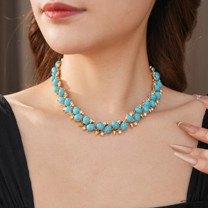 Gros plan d'un collier vintage doré avec turquoise et strass porté par un modèle