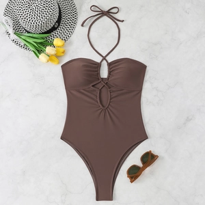 Détail d'un monokini marron foncé ajouré avec dos nu et plissé sur fond de marbre blanc