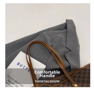 Detalle de bolso tote con monograma, asas de cuero, remaches dorados y un blazer gris chic