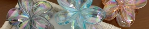 Close-up of translucent plumeria flower hair claws with colorful holographic finishes