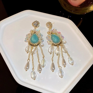 Detail of long tassel earrings with green gemstones and white pearls on white tray