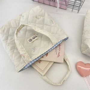 Detail of white quilted canvas tote with embroidered bows and blue checkered lining
