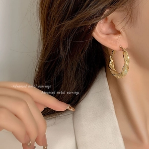 Close-up of elegant gold twisted hoop earrings worn by a model in casual white shirt