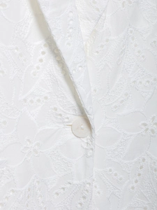 Détail du blazer blanc avec broderie anglaise délicate et un bouton en nacre élégant