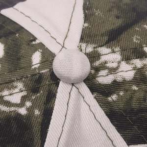 Close-up of baseball cap top button with green camo stitching and white twill fabric