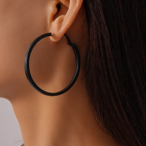 Close-up of a model wearing large black matte geometric round leather hoop earrings