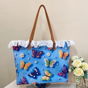 Detail of blue canvas backpack featuring colorful butterfly embroidery and white fringe trim