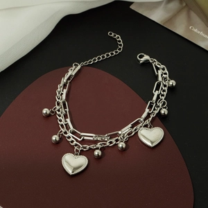 Silver double-layered bracelet with heart pendants and beads on a red leather pad