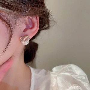 Detail shot of a model wearing a geometric gold earring with rhinestones and large pearl
