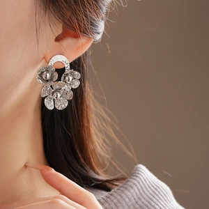 Detailed close-up of textured silver flower earrings worn by a model in soft lighting