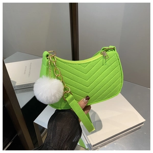 Détail du sac matelassé vert vif avec chaîne dorée et pendentif boule en peluche blanche