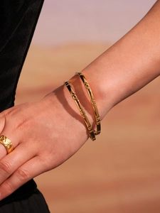 Detail of stacked bamboo texture gold bangles on model with warm sand background
