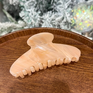Detail of light pink acetate hair claw clip with marble texture on a wooden tray
