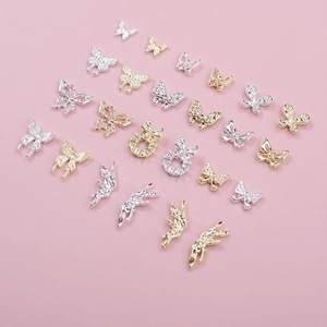 Macro shot of gold and silver butterfly nail charms with rhinestones on pink background