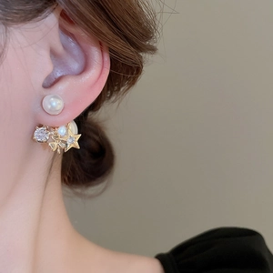 Close-up of gold star and pearl drop earrings worn by a model in a luxury setting